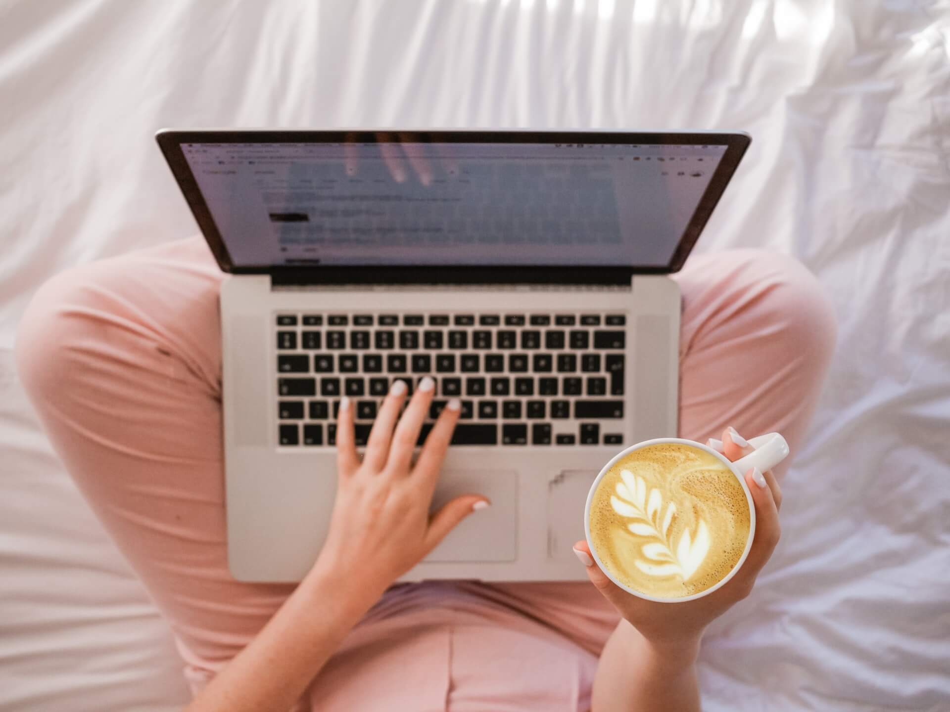 Woman with laptop on her lap holding a latte