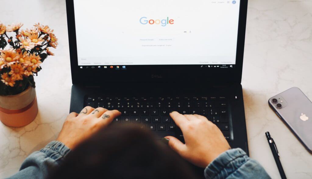 Hands typing on laptop. Computer displays Google home page.