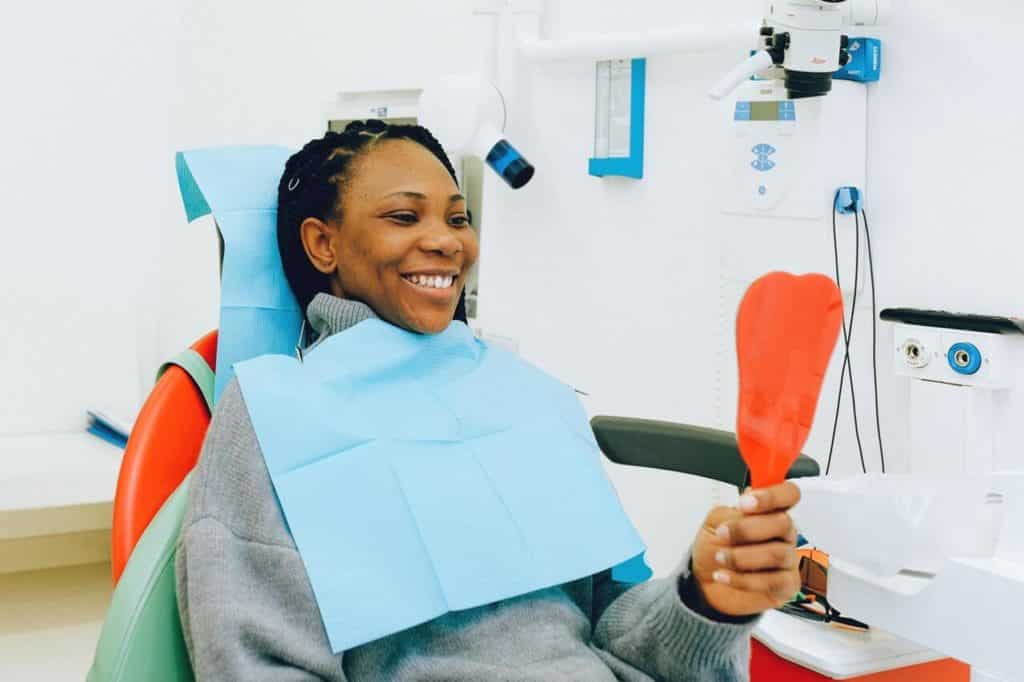Girl in dentist chair looking in mirror and smiling
