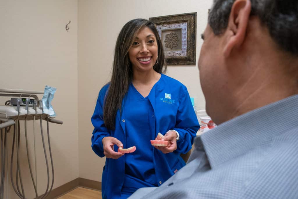 Hygienist showing dentures to dental patient.