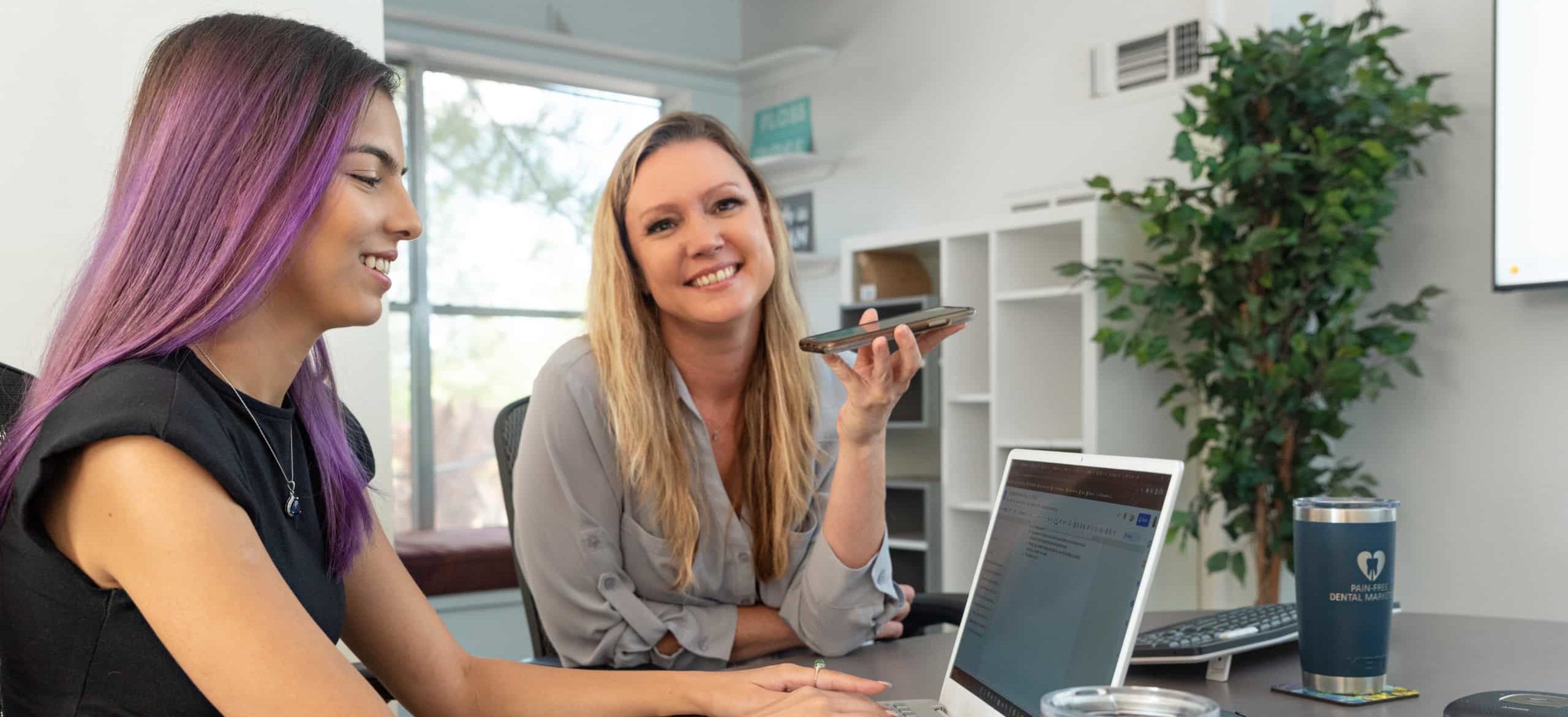 Two Pain-Free Dental Marketing team members working on laptop and talking on the phone.