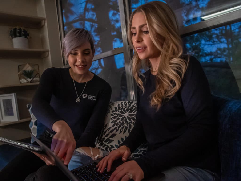 Two Pain-Free team members looking at laptop and pointing